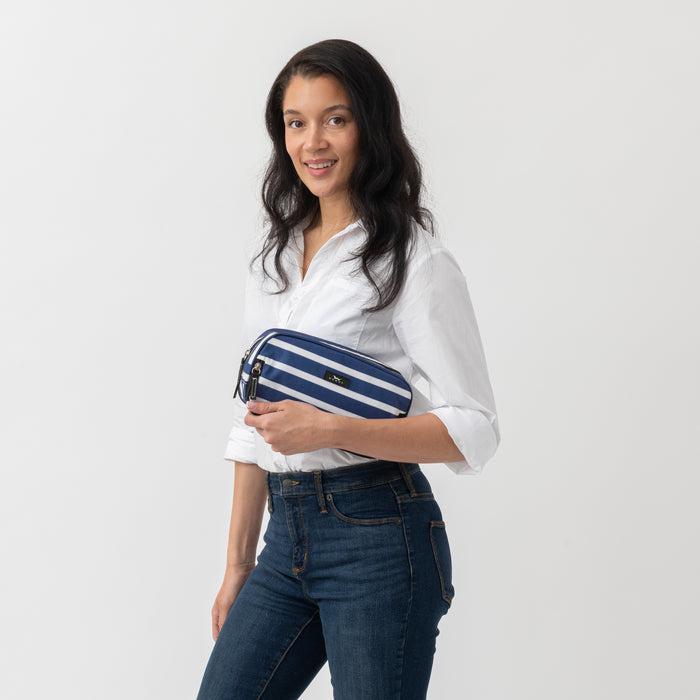 Woman holding a blue and white striped pouch against a plain background