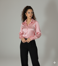 Woman wearing a pink satin shirt and black pants against a gray background