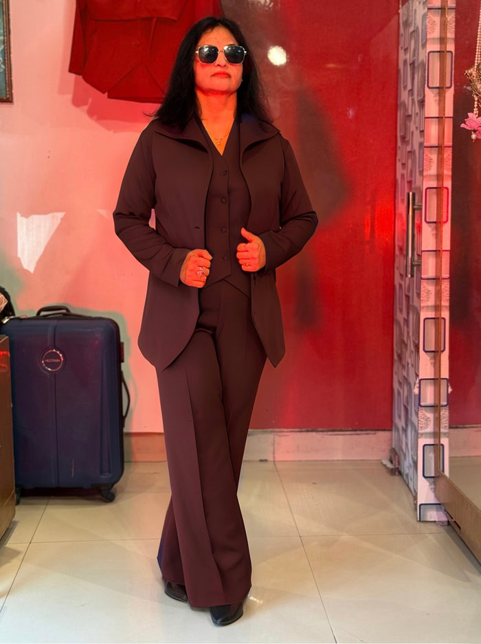 Person wearing a brown suit standing next to a suitcase in a room with red walls.