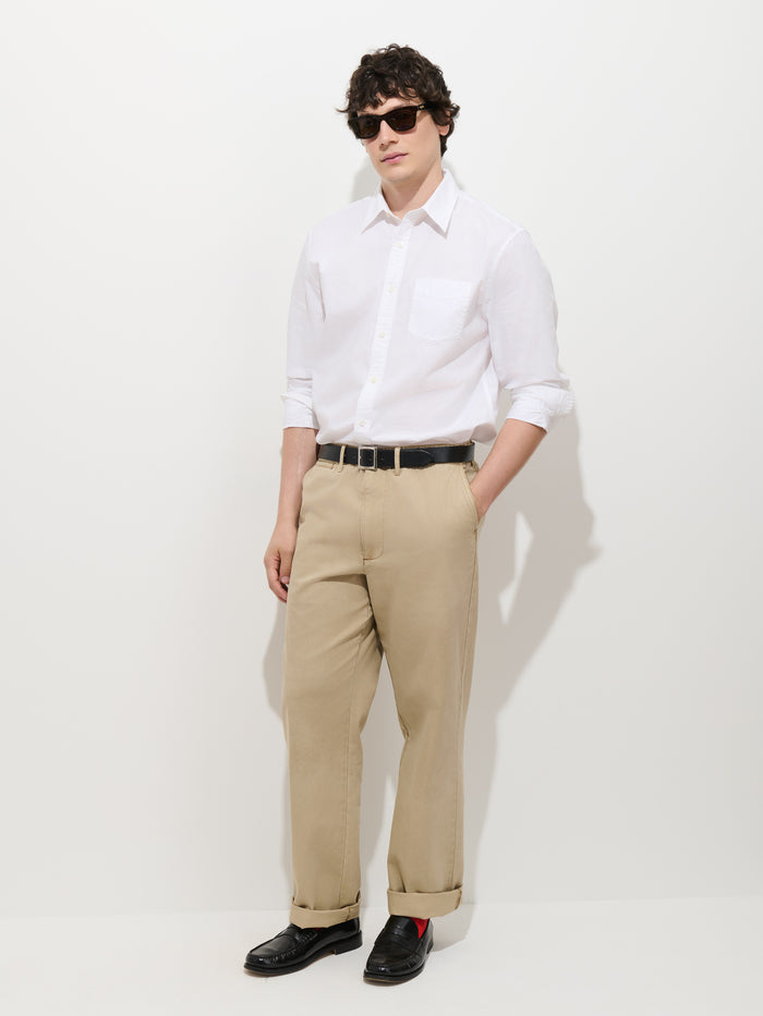 A person wearing a white button-up shirt, the Flat Front Chino in Vintage Wash, a black belt, black shoes, and sunglasses stands against a plain white background with hands in pockets.