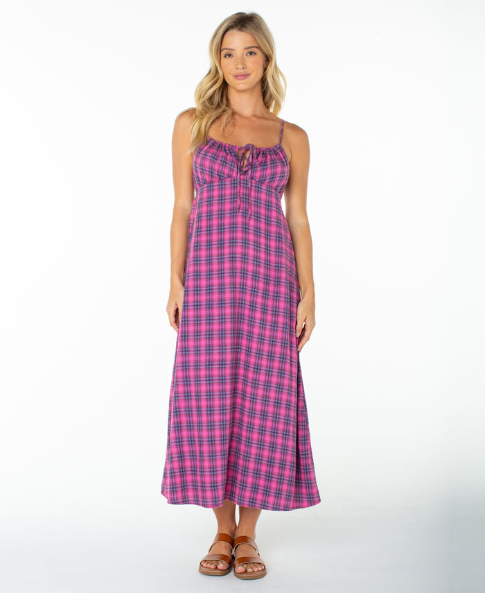 A woman wearing the Roxy Late Night Midi Dress in Naval Academy Sunburst Plaid—a long, sleeveless midi dress with spaghetti straps and a ruched drawstring neckline—paired with brown sandals, stands against a plain white background.