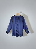 Navy blue satin shirt on a hanger against a red wall with gold poles.
