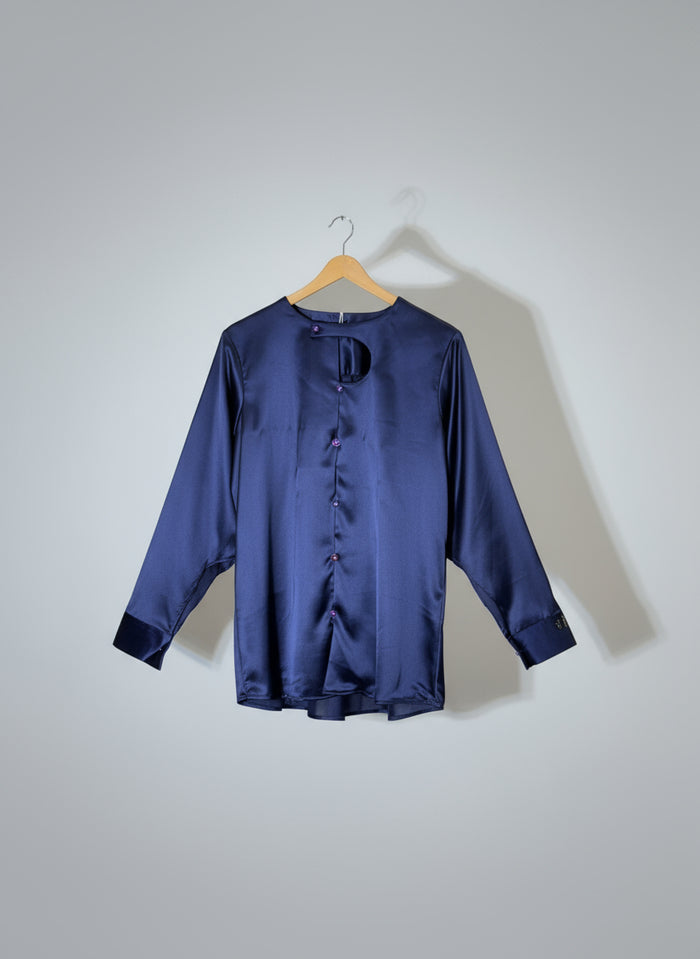 Navy blue satin shirt on a hanger against a red wall with gold poles.