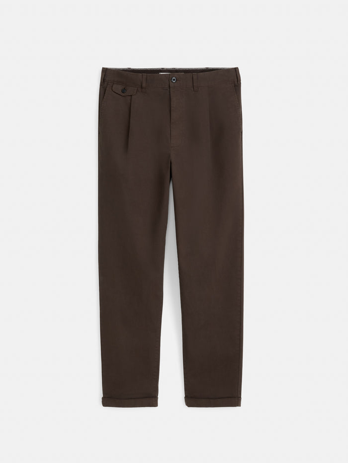 The Standard Pleated Pant in Chino is a pair of brown straight-leg pants featuring front pleats, a button and zip closure, side and back pockets, and crafted from soft cotton twill, shown laid flat on a white background.