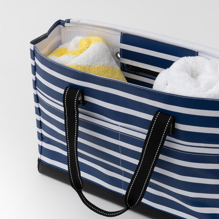 Blue and white striped tote bag with towels inside on a light gray background